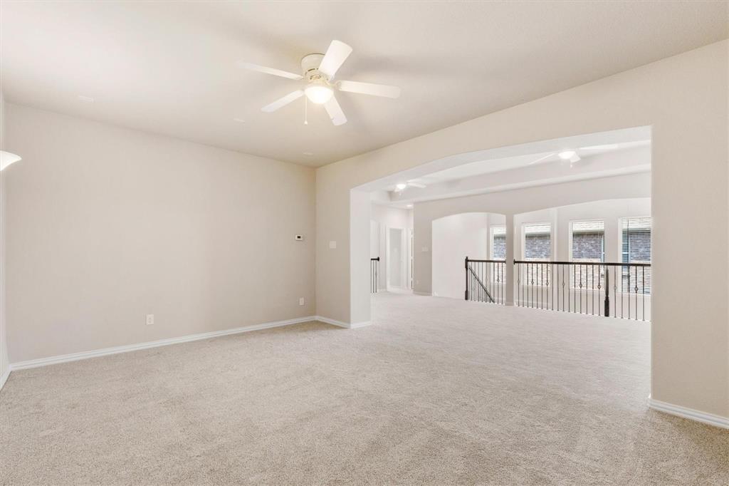 Neutral carpeting, ceiling fan with integrated light fixture, arched architectural detailing, and decorative metal balusters