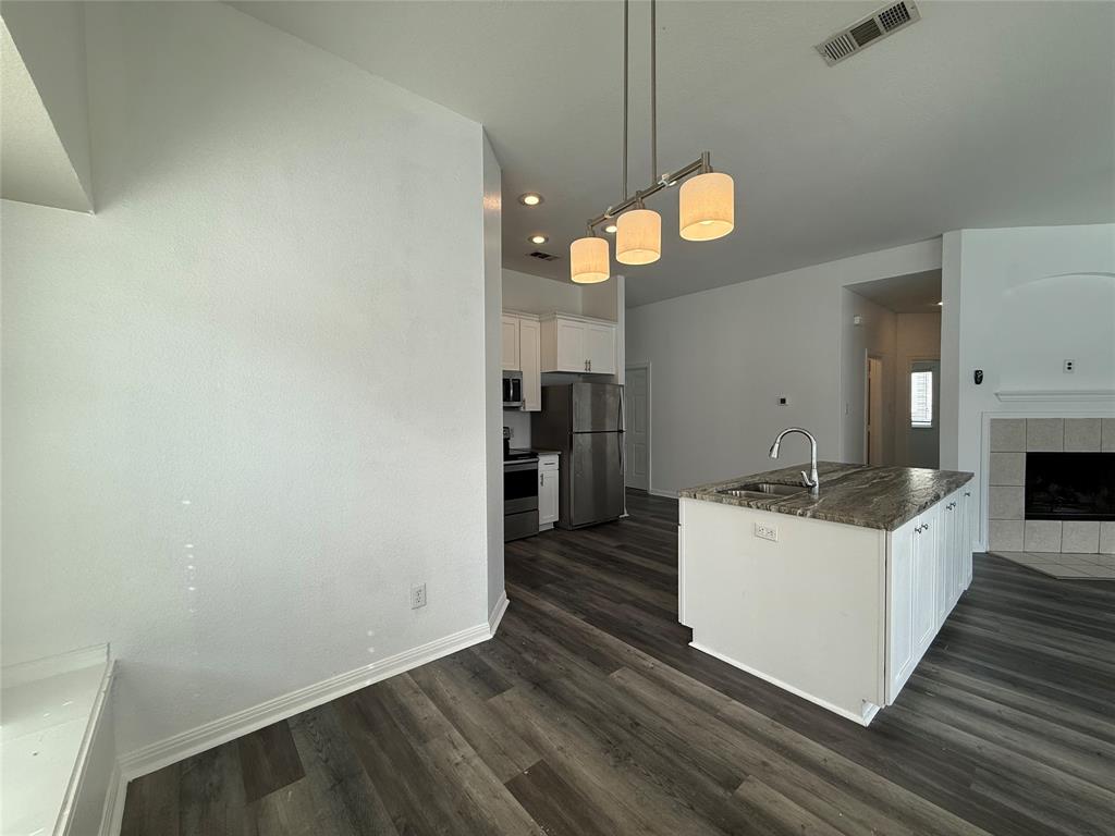 Kitchen featuring a stone-topped center island with a stainless steel faucet, wood-finish flooring, recessed lighting, and a three-bulb pendant fixture