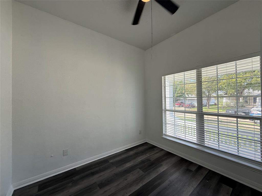 Room featuring wood-finish flooring, high ceilings, a ceiling fan, and a large window with horizontal blinds