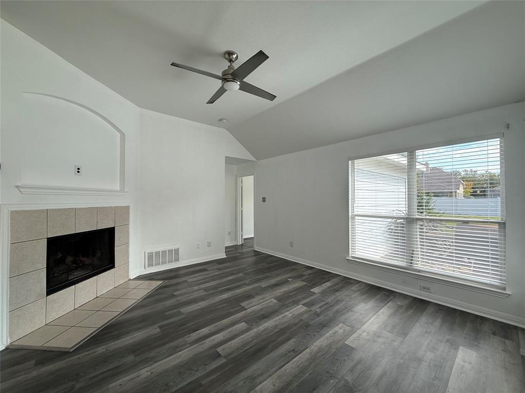 Vaulted ceilings, wood-finish flooring, corner fireplace with tile surround, and large window with blinds