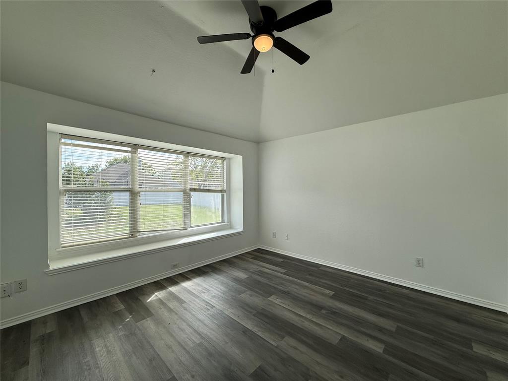 Vaulted ceiling featuring a central multi-blade ceiling fan, wide bay window with built-in ledge, and wood-finish flooring