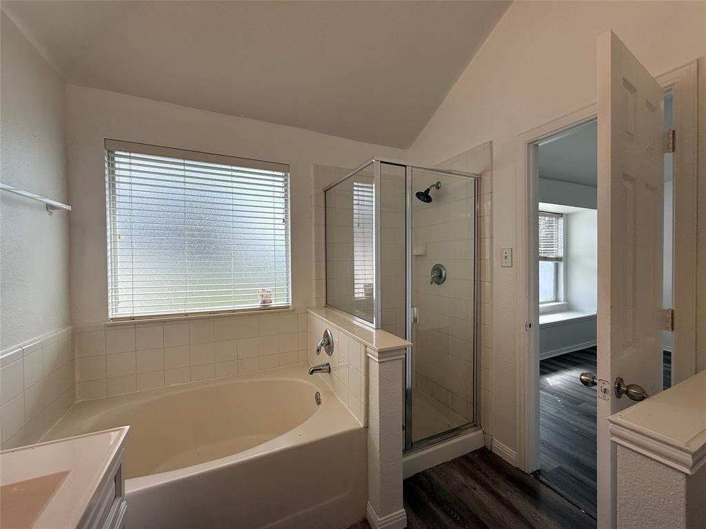 Soaking tub with tiled surround, glass-enclosed shower, sloped ceiling, and wood-finish flooring