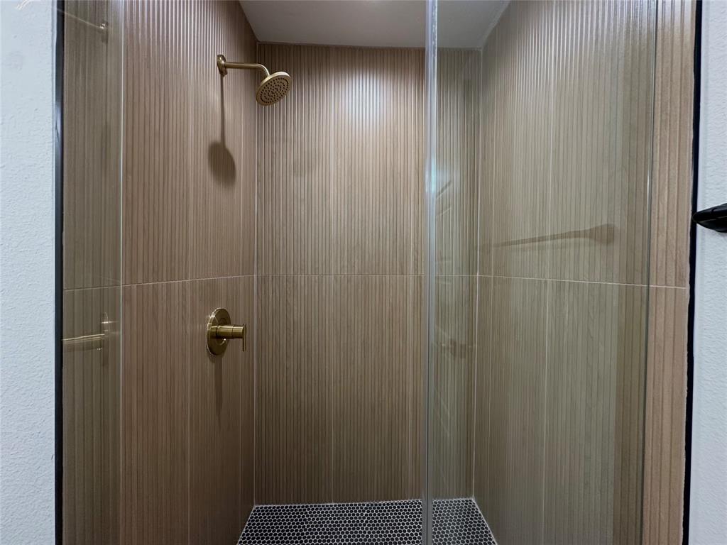 Shower enclosure featuring floor-to-ceiling vertical textured tile, hexagonal mosaic floor tile, brass-finish fixtures, and a glass door