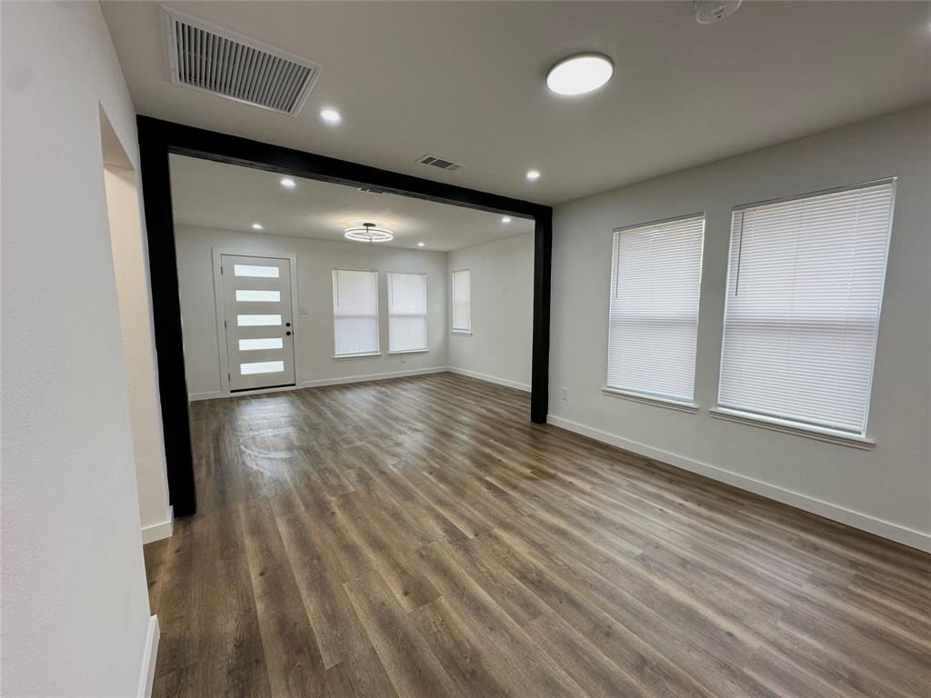 Wood-finish flooring, high-contrast dark architectural framing, recessed lighting, multi-panel glass insert entry door, and large windows