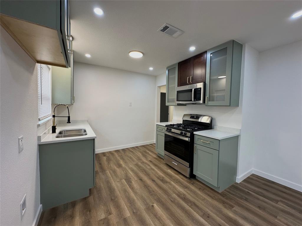 Kitchen featuring sage green cabinetry, stone-finish countertops, stainless steel gas range, integrated microwave, and wood-finish flooring