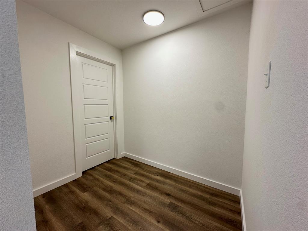 Neutral-toned interior space featuring wood-finish flooring, a five-panel interior door, and a flush-mount ceiling light fixture