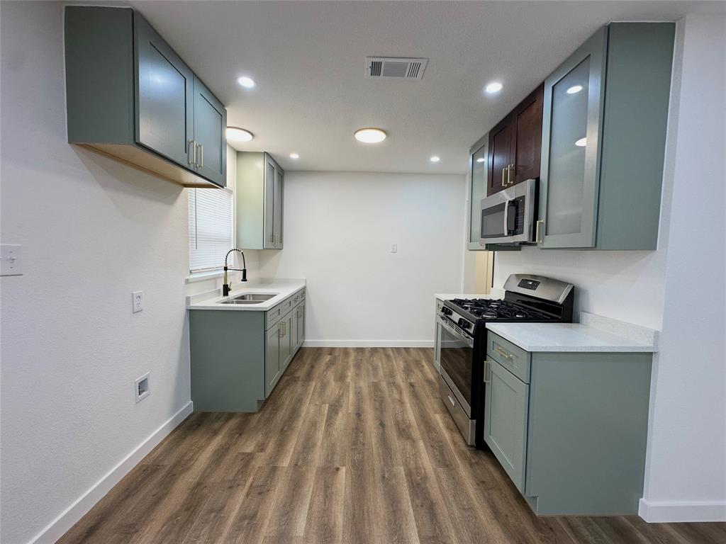 Kitchen featuring custom cabinetry with frosted glass inserts, stone-finish countertops, stainless steel appliances, wood-finish flooring, and recessed lighting