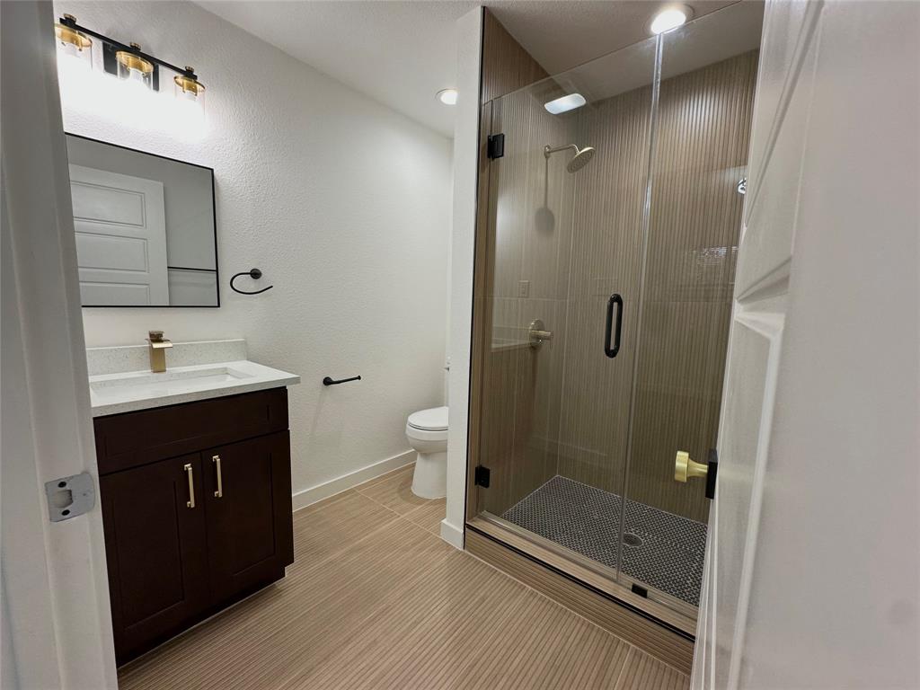 Bathroom featuring a dark wood-finish vanity with a light-toned countertop, a frameless glass-enclosed shower with floor-to-ceiling tile, and modern metallic fixtures