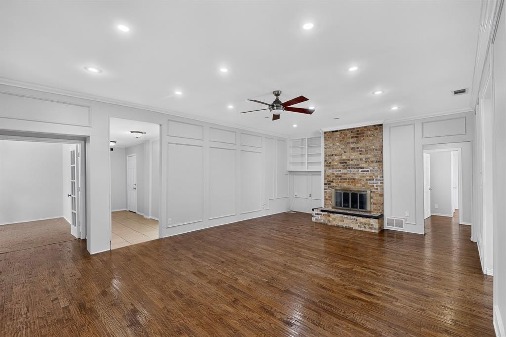 Hardwood flooring throughout, featuring a brick-face fireplace with hearth, built-in shelving, recessed ceiling lighting, and crown molding Hardwood flooring throughout, featuring a brick-face fireplace with hearth, built-in shelving, recessed ceiling lighting, and crown molding
