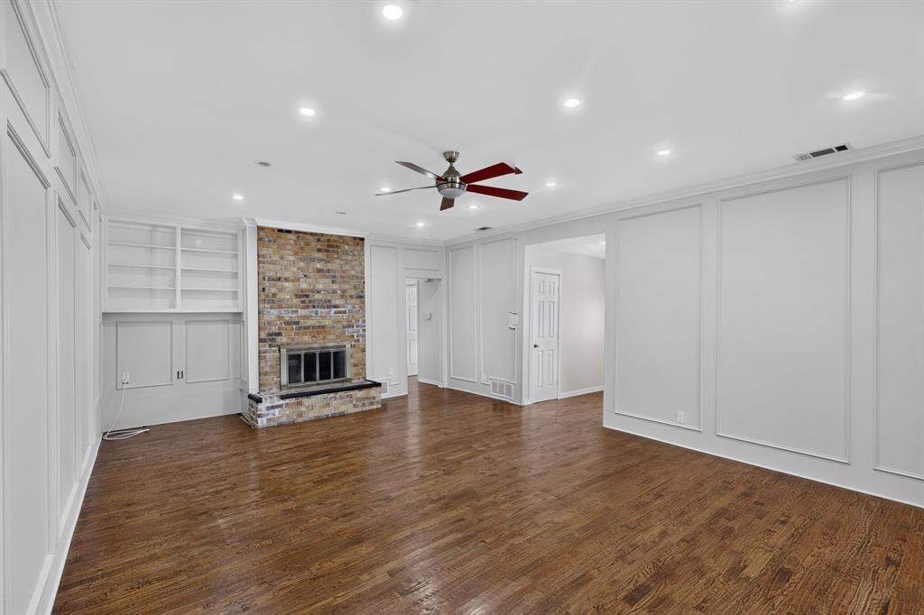 Wood flooring, recessed lighting, brick fireplace with a black hearth, built-in shelving, and decorative wall paneling Wood flooring, recessed lighting, brick fireplace with a black hearth, built-in shelving, and decorative wall paneling