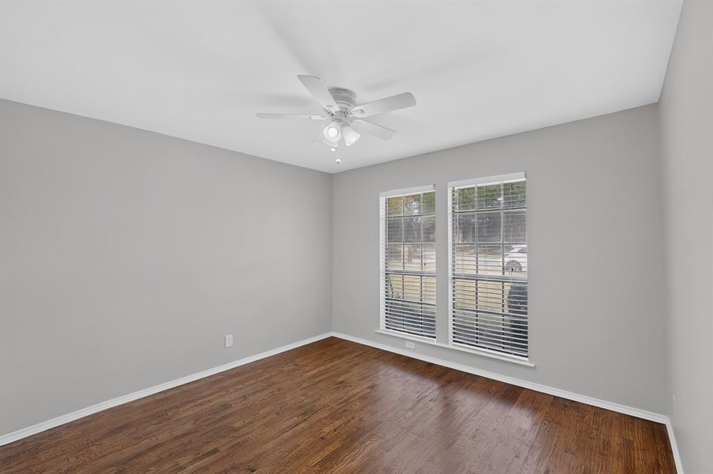 Wood-finish flooring, light gray walls, white ceiling fan, and two large windows with blinds