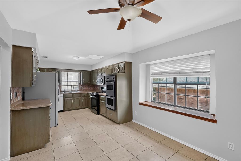 Spacious kitchen featuring stainless steel appliances, wood-finish cabinetry, tile flooring, and abundant natural light from large windows with wood-trimmed sills and window seat Spacious kitchen featuring stainless steel appliances, wood-finish cabinetry, tile flooring, and abundant natural light from large windows with wood-trimmed sills and window seat