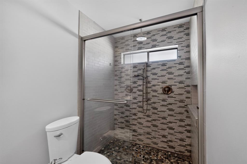 Glass-enclosed shower with a rain shower head, handheld shower, stone pebble flooring, and a tiled accent wall