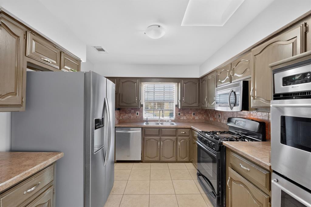 Kitchen featuring wood-finish cabinetry, tile flooring, stainless steel appliances, and a built-in microwave Kitchen featuring wood-finish cabinetry, tile flooring, stainless steel appliances, and a built-in microwave