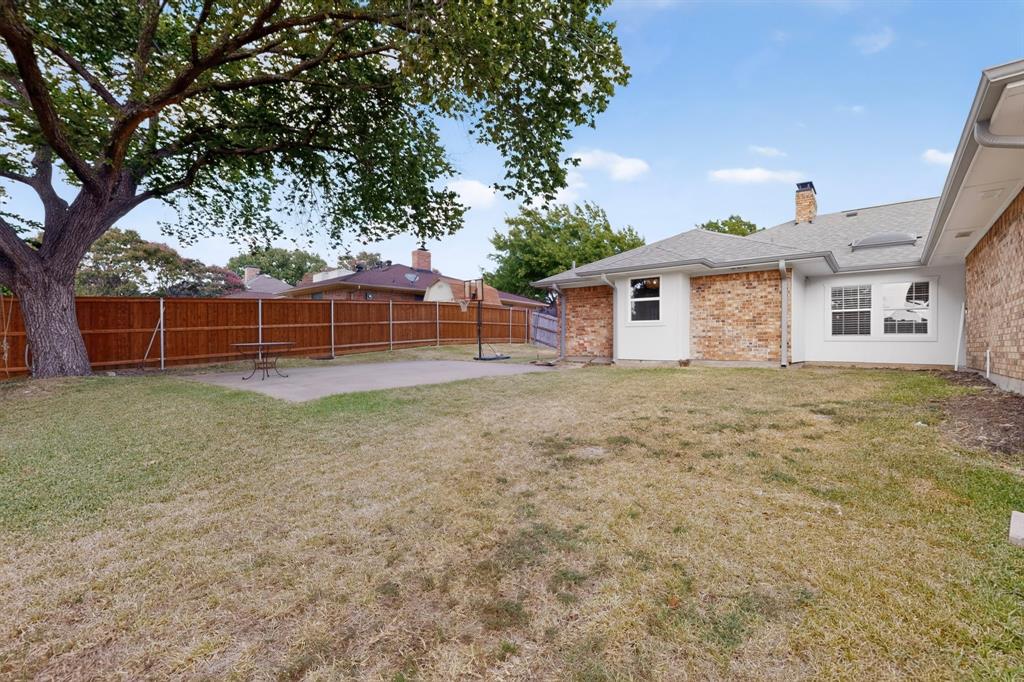Expansive backyard featuring a mature tree, privacy fencing, concrete patio, and brick exterior