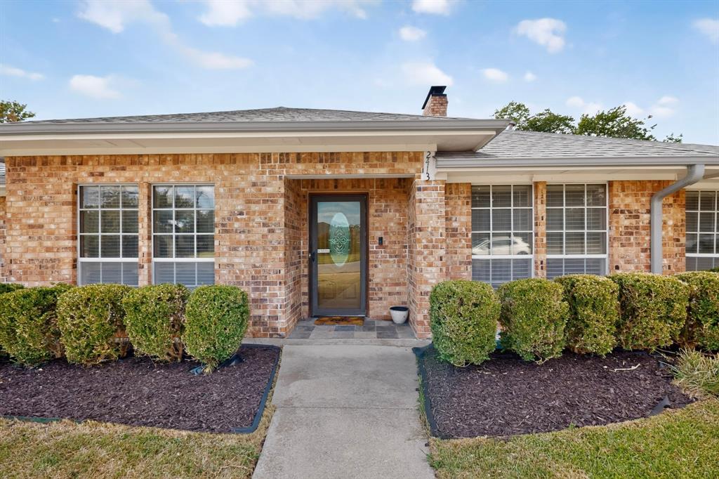 Brick exterior with multiple windows, a central entry door with decorative glass, and a concrete walkway Brick exterior with multiple windows, a central entry door with decorative glass, and a concrete walkway