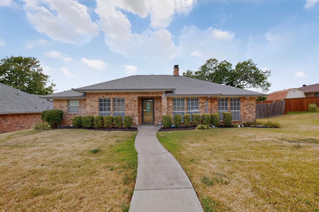 Brick exterior with a gray shingle roof, established landscaping, and a concrete pathway leading to the front entry