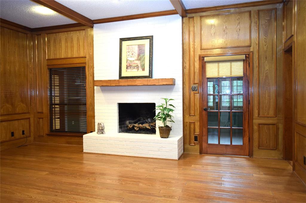 Wood paneling with recessed molding, white-painted brick fireplace, timber beam ceiling accents, wood-finish flooring, and French glass door with wood trim