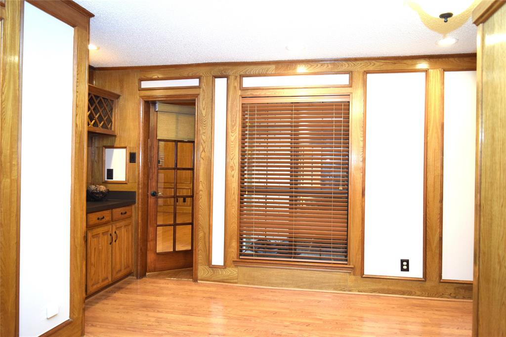 Interior room featuring wood-finish paneling, built-in cabinetry with integrated wine storage, wood-finish flooring, a glass-paned interior door, and a window fitted with slatted blinds