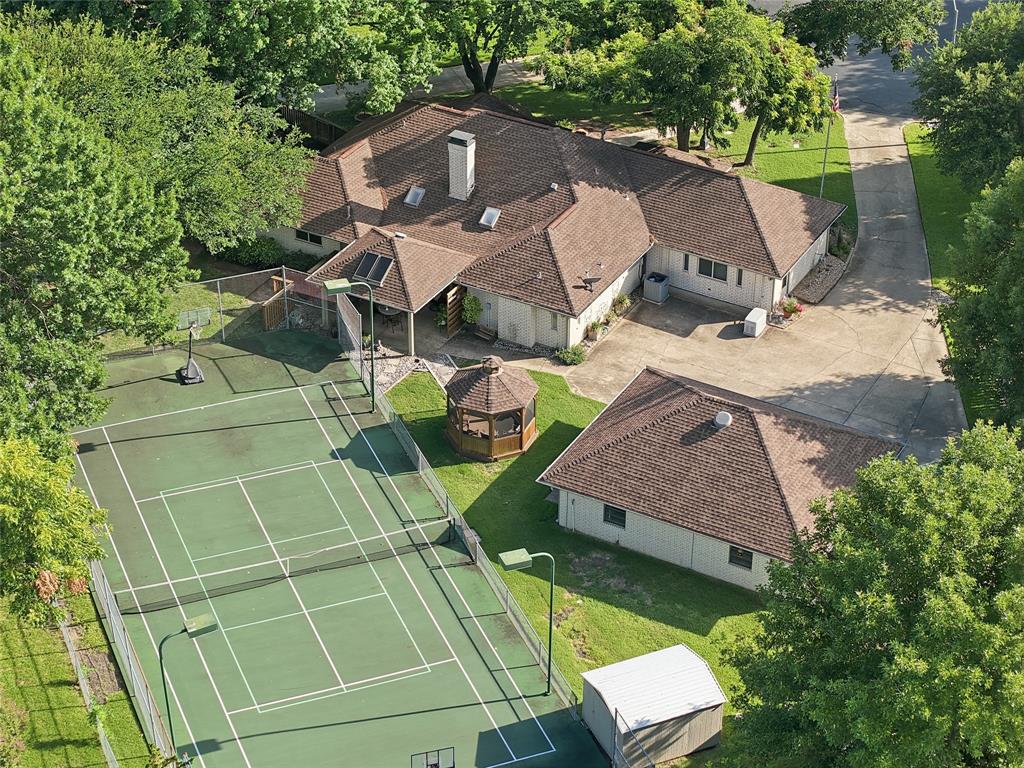 Aerial perspective featuring a hard-surfaced tennis court, detached garage, gazebo, concrete driveway, and sprawling tree-lined grounds