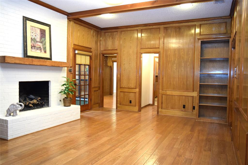 Wood-paneled wall detailing, white-painted brick fireplace with a wood mantle, built-in shelving, and wood-finish flooring