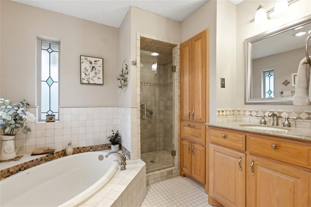 Bathroom featuring a jetted soaking tub, tiled shower enclosure with a glass door, custom wood cabinetry, stone-finish vanity countertop, and a vertical window with stained glass detailing