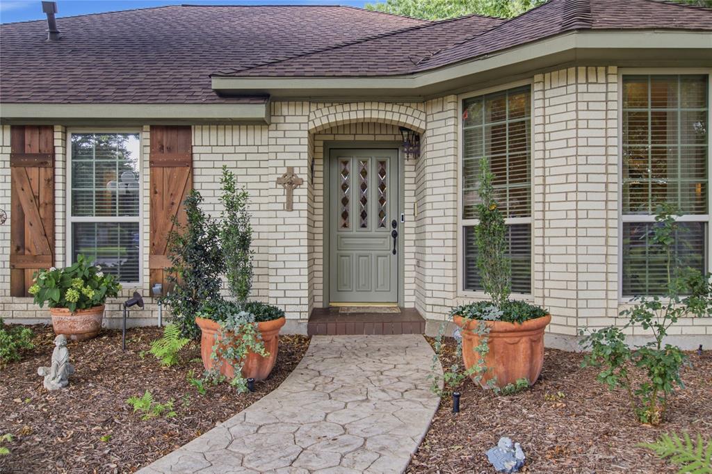 Light brick facade featuring decorative wood-finish shutters, a covered entryway, and a patterned concrete walkway Light brick facade featuring decorative wood-finish shutters, a covered entryway, and a patterned concrete walkway