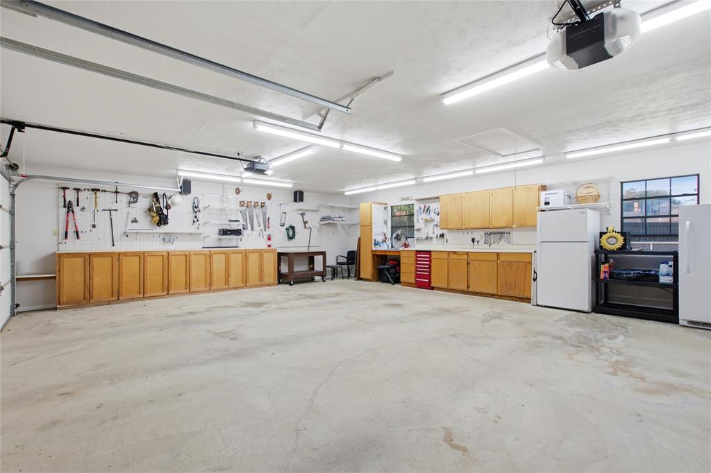 Spacious garage featuring extensive built-in wood-finish cabinetry, concrete flooring, overhead LED lighting, and a multi-pane window
