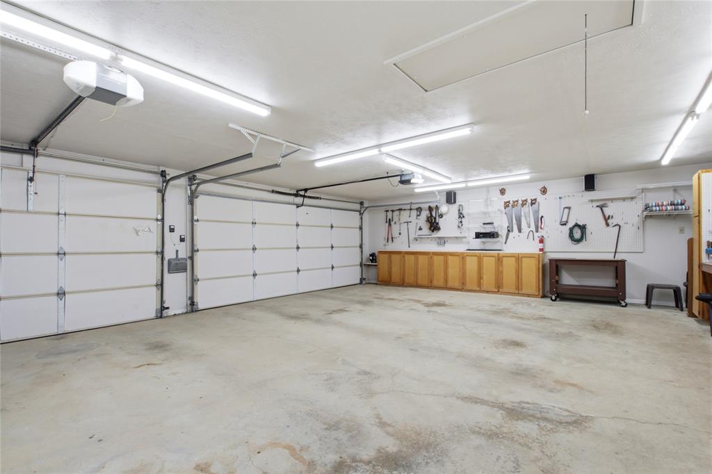Spacious three-car garage featuring two white sectional doors, built-in wooden cabinetry, recessed wall-mounted tool storage, and integrated linear fluorescent lighting