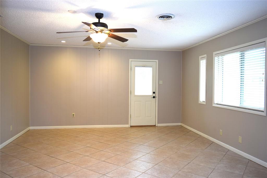 Neutral-toned interior space featuring light-colored tile flooring, panel-textured walls, a ceiling fan with integrated lighting, and natural light provided by multiple windows