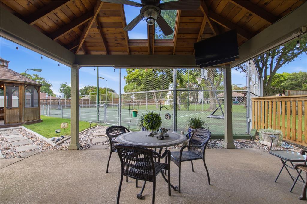 Covered patio featuring a wood-plank ceiling, skylights, an overhead ceiling fan, concrete flooring, and an fenced-in tennis court