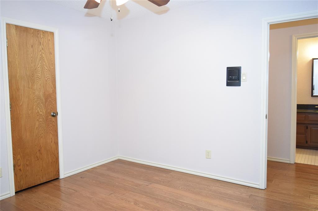 Room with wood-finish flooring, solid wood-finish door, and ceiling fan with integrated lighting