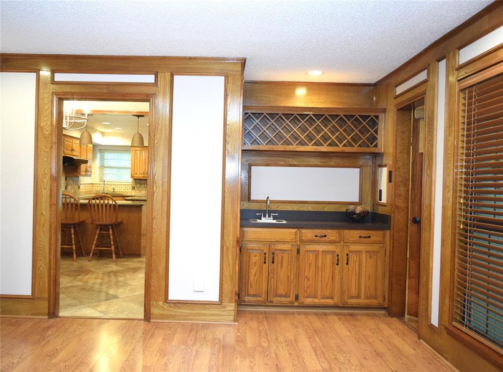 Custom built-in bar featuring wood cabinetry, integrated lattice wine storage, countertop, sink, and wood-finish flooring