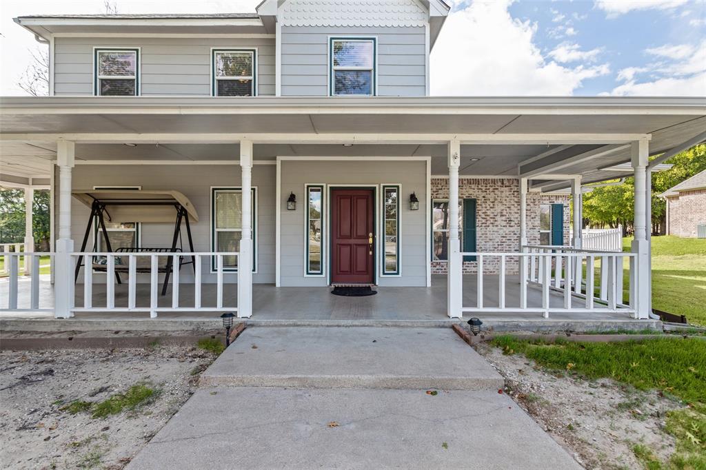 Two-story residence featuring horizontal lap siding, a wrap-around covered porch with white railing, a brick facade accent, and a solid-core front door with sidelights