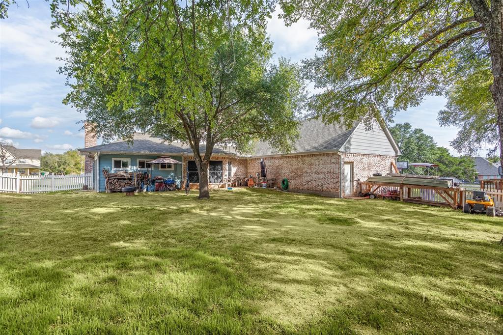 Expansive backyard featuring a brick and siding exterior, mature shade trees, a white picket fence, and a wooden deck structure