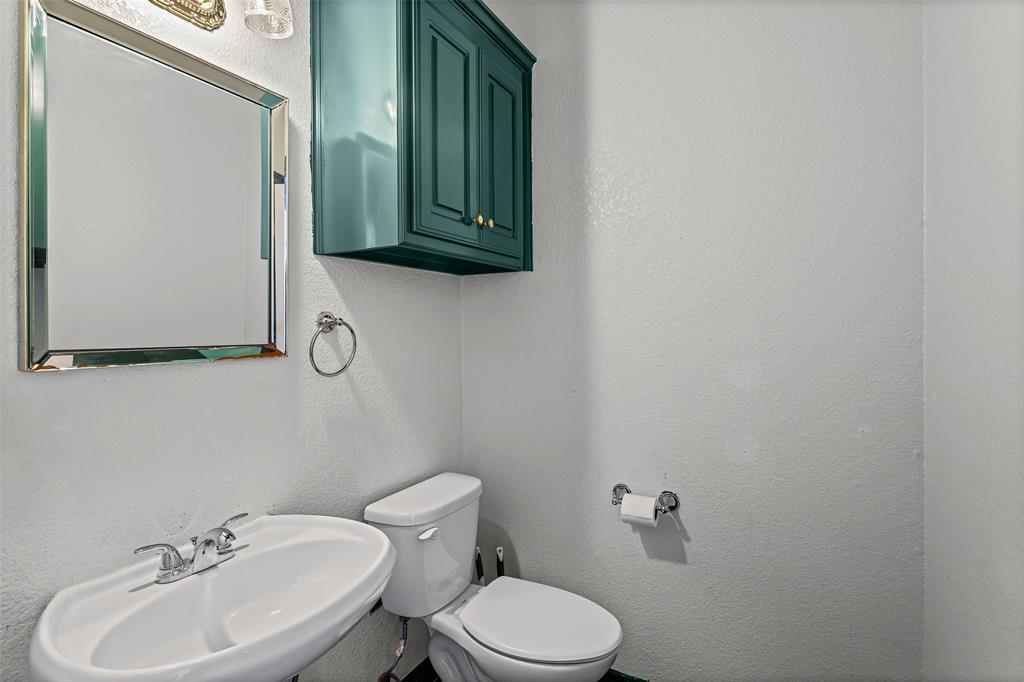 Wall-mounted teal cabinetry, pedestal sink with dual-handle faucet, chrome-framed mirror, and chrome towel hardware
