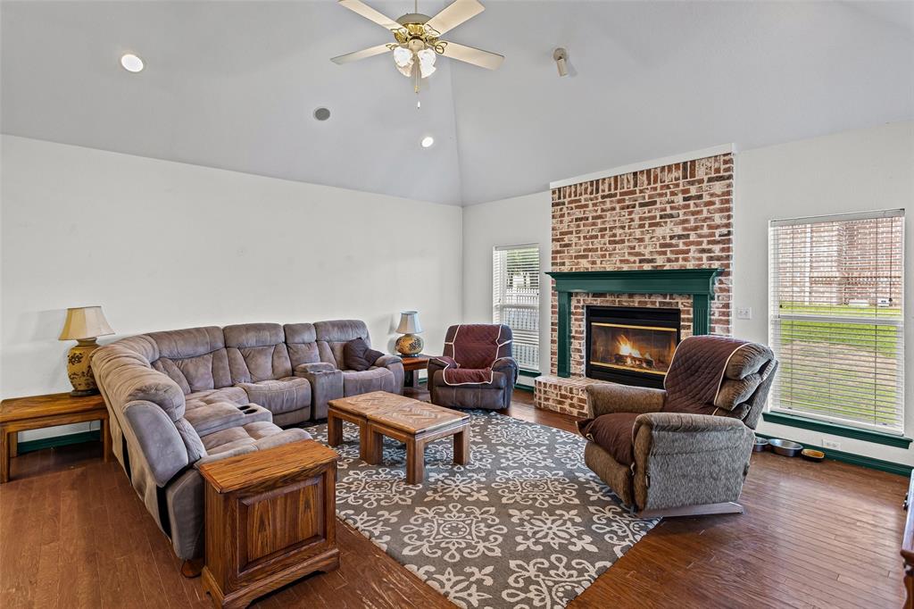 Vaulted ceiling with a central ceiling fan, brick-surround fireplace, dark wood-finish flooring, and natural light via large windows