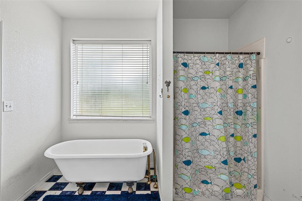 Freestanding clawfoot tub with metallic hardware, checkered tile flooring, and a window featuring horizontal blinds