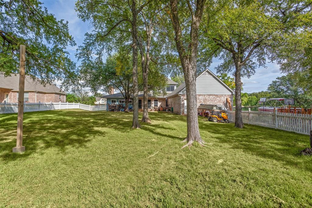 Spacious backyard featuring mature trees, a white vinyl privacy fence, and brick and horizontal siding exterior finishes