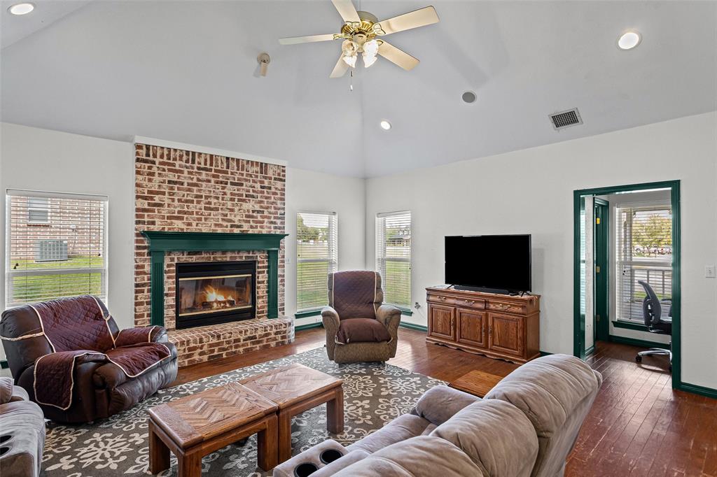 Vaulted ceiling, brick fireplace with a custom mantle, wood-finish flooring, and recessed lighting