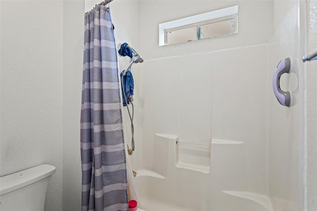 Bathroom featuring a one-piece molded tub and shower surround with built-in soap ledges, adjustable handheld shower fixture, and a transom window