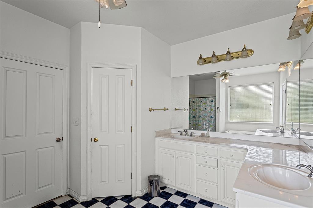 Dual-sink vanity with white cabinetry, expansive wall-to-wall mirror, multi-light vanity fixtures, and checkerboard patterned flooring