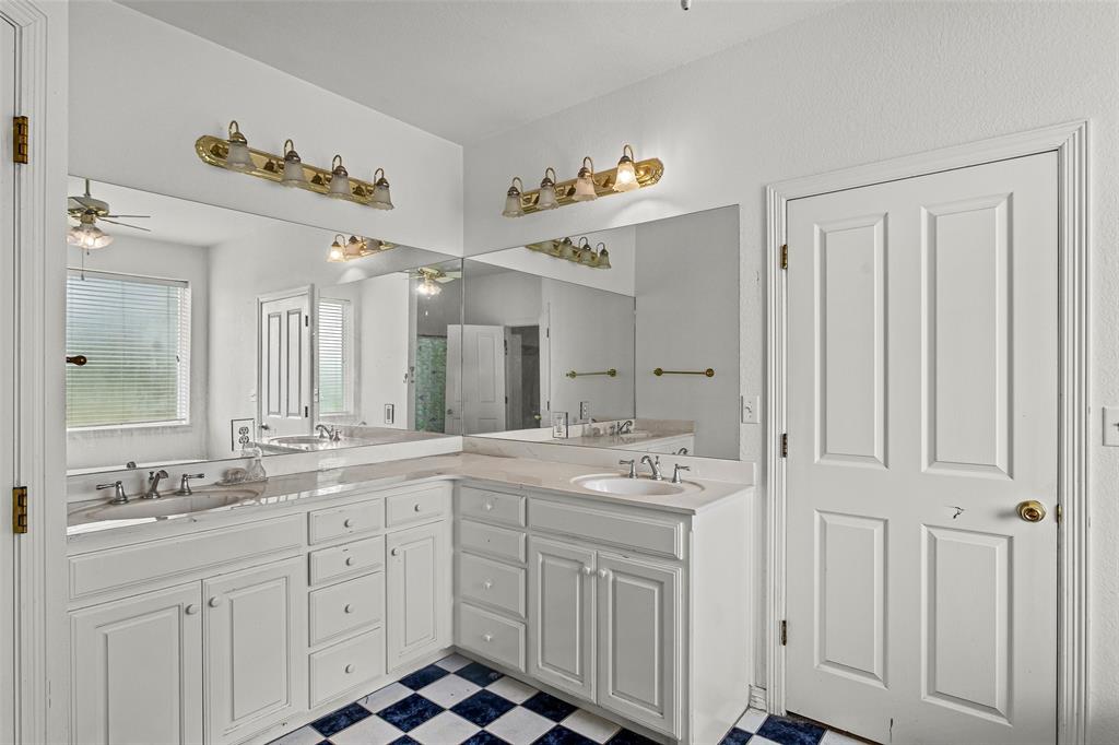 L-shaped vanity featuring white cabinetry, dual undermount sinks, stone countertops, expansive wall-to-wall mirrors, and checkered tile flooring