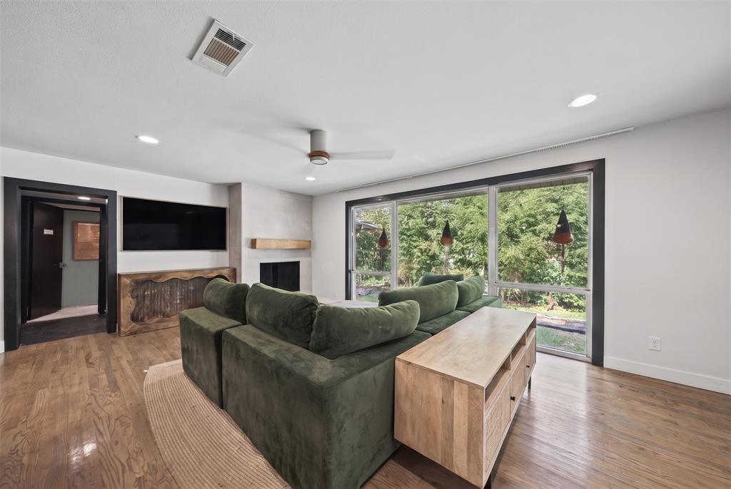 Living area featuring wood-finish flooring, floor-to-ceiling glass wall, stone-surround fireplace with wood mantel, and recessed ceiling lighting