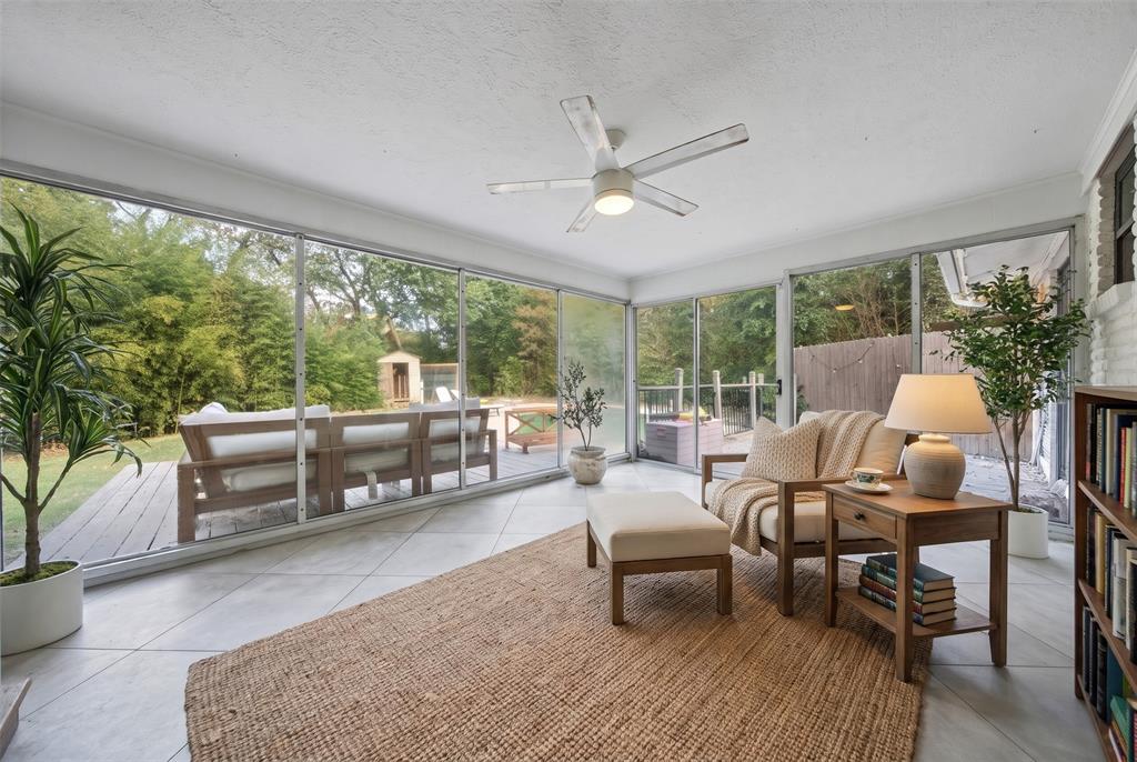 Enclosed sunroom featuring expansive glass walls, large-format tile flooring, a central ceiling fan, and built-in shelving