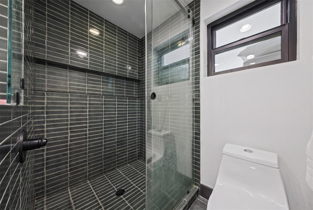 Walk-in shower featuring dark grey vertical tile surround, recessed wall niche, frameless glass enclosure, and black hardware, complemented by a dual-flush toilet