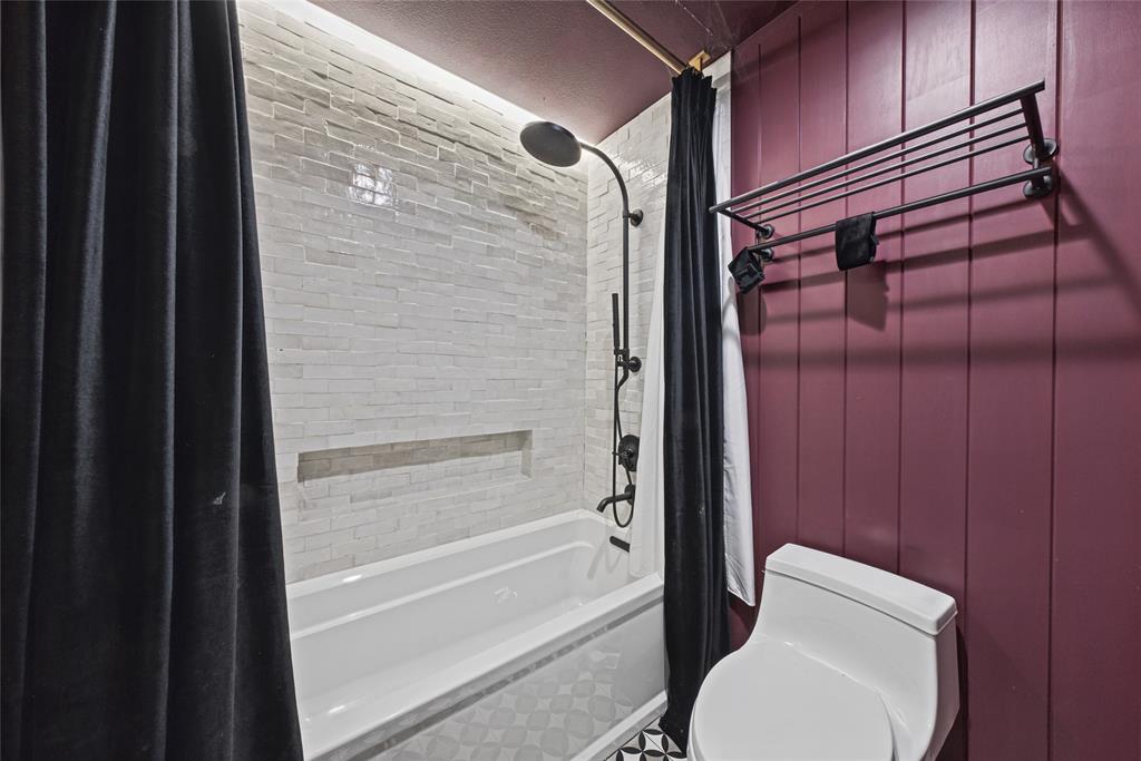 Bathtub featuring textured tile surround with recessed niche, matte black rainfall shower system, vertical wood-panel wall, and wall-mounted metal shelving