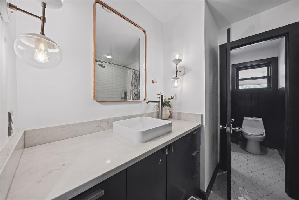 Modern vanity with a light-toned solid surface countertop and rectangular vessel sink, paired with a copper-trimmed mirror, glass globe wall lighting, and hexagonal tile flooring
