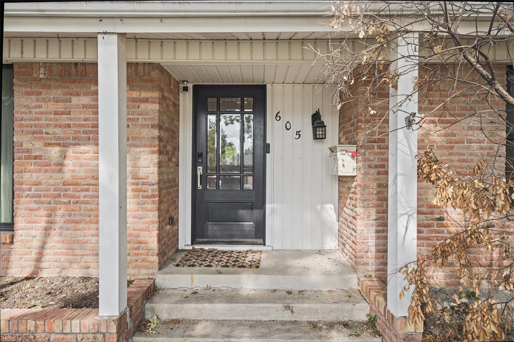 Covered front entryway featuring a masonry brick facade, vertical paneling, a multi-pane glass-inlay door, and an attached exterior light fixture