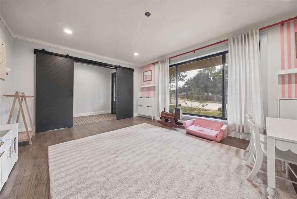 Interior space featuring wood-finish flooring, large picture window with track-mounted drapery, and dual matte black chevron-pattern sliding barn doors